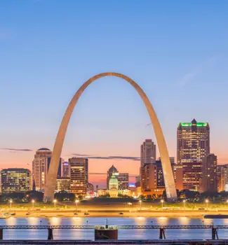 The Gateway Arch in St. Louis, Missouri on a cloudy day in front of the city and buildings.