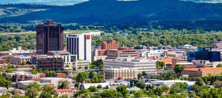 City of Billings, Montana aerial view of buildings surrounded by green tress and mountains with a large cloud shadow.