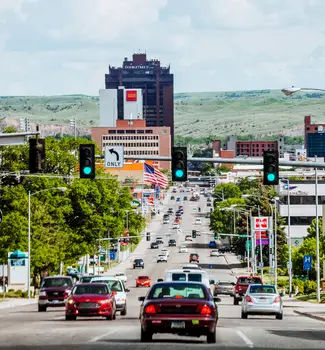 Streets of billings, Montana with traffic and cars leading down into the city lined with buildings and traffic lights.