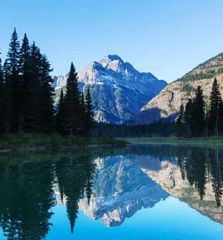 Glacier National Park mountain reflected on a calm water lake surrounded by evergreen trees in Montana.