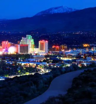 View of Reno, Nevada at night with buildings lit up in different colors with mountains in the background.