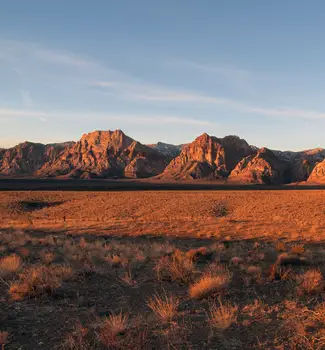 Red Rock Valley in Nevada with flat sandy land in front of warm-colored rocky mountains.