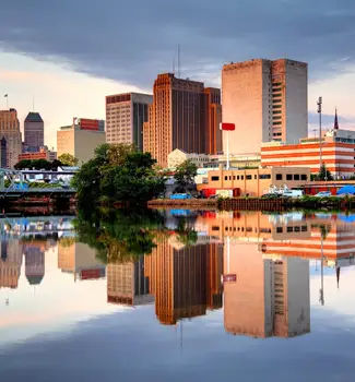 Downtown Newark, New Jersey city waterfront with buildings reflecting off the calm waters at dusk.