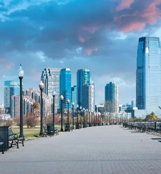 Liberty State Park in New Jersey City with light posts in a row leading into the city along a brick paved road at dusk.