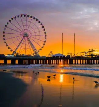 Ferris wheel on a dock at the Steel Pier in Atlantic City, New Jersey at sunset with birds and a beach in the foreground.