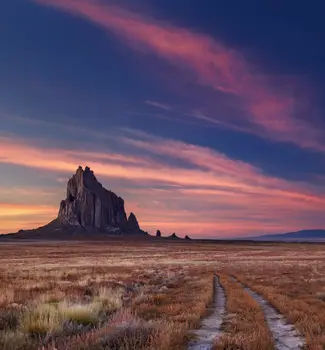Shiprock the great volcanic rock mountain in the desert plane of Santa Fe at sundown surrounded by dry grass tufts.