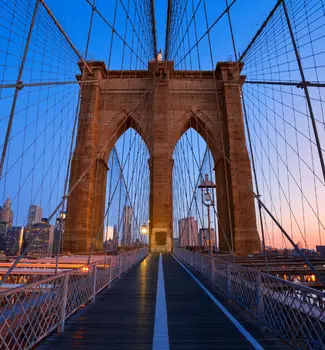 Looking down Brooklyn Bridge in New York during sunset with dark blue skies and warm yellow tones.