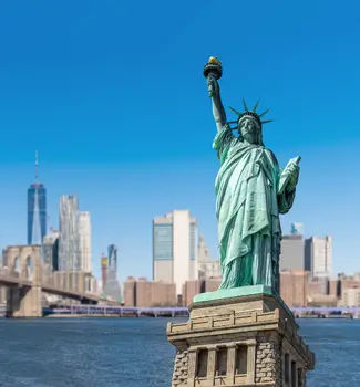 Statue of Liberty with New York City landscape skyscrapers behind Brooklyn Bridge.