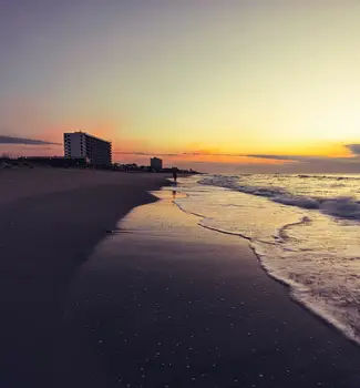 Sunset at a North Carolina Beach with buildings far in the distance and water creeping up the sandy shore.