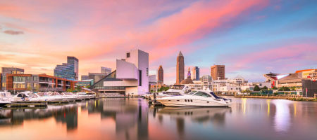 Waterfront city view of Cleveland, Ohio with plenty of yachts, boats, and ships on a lake during sunrise or sunset with a colorful sky.