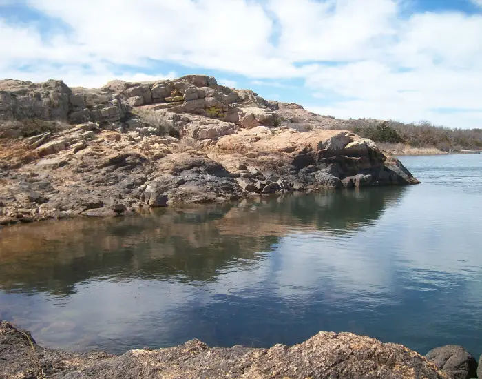 Oklahoma lake on a sunny day with clouds of crystal clear waters between rocky landscapes.