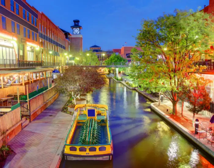 Bricktown Canal in Oklahoma City, the entertainment district at night with a touring boat and river between shopping buildings.