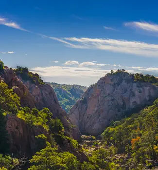 View of mountains in Oklahoma with tops sprinkled with green trees and a partly cloudy sky during the day.