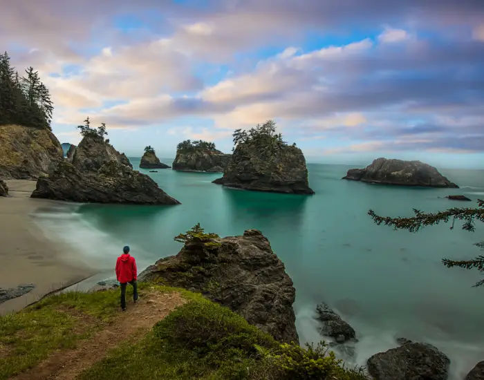 Man wearing a bright red jacket looking out into Oregon coastline views from a rock on the beach.