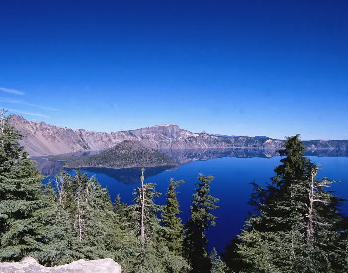 Aerial view of Crater Lake during the winter surrounded by mountains and evergreen trees.