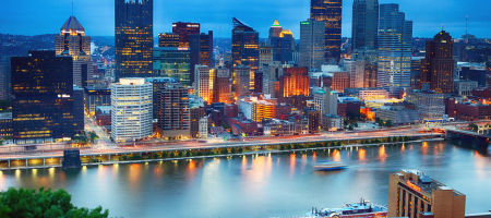 Downtown Pittsburgh, Pennsylvania waterfront skyline in the evening with lit up buildings reflecting off the water.