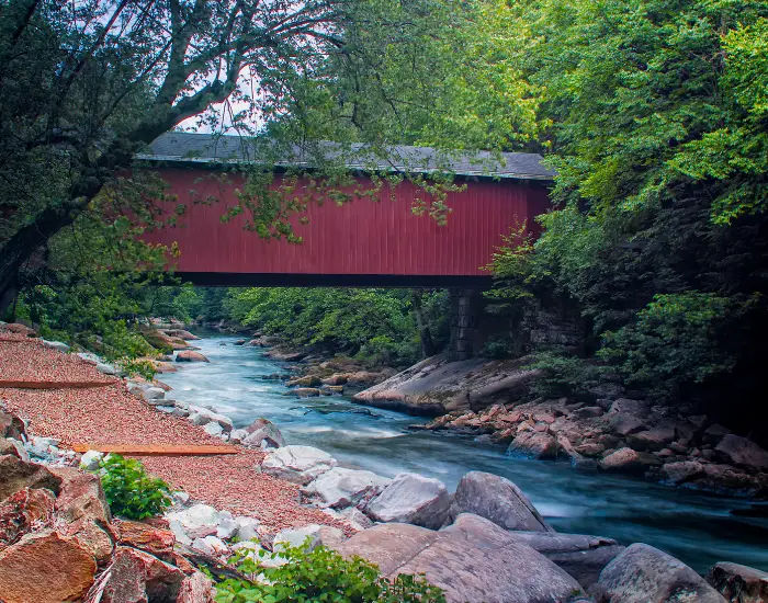 Covered red bridge in McConnell's Mill, Pennsylvania with a river trail flowing under.