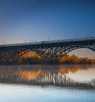 Schuylkill River in Pennsylvania at dusk close to night with a bridge stretching across the waters and warm autumn trees in the background.