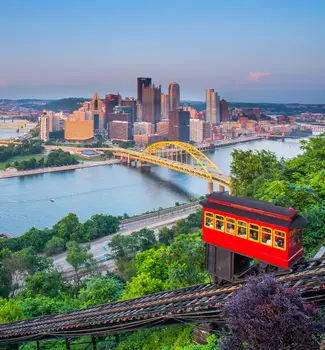 Red sky carriage going up a mountain in Pittsburgh, Pennsylvania with scenic sights of Monogahela River and a bridge crossing into the city over water.