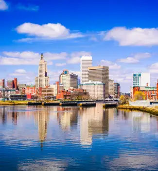 Providence, Rhode Island skyline in front of a lake on a partly cloudy sunny day.