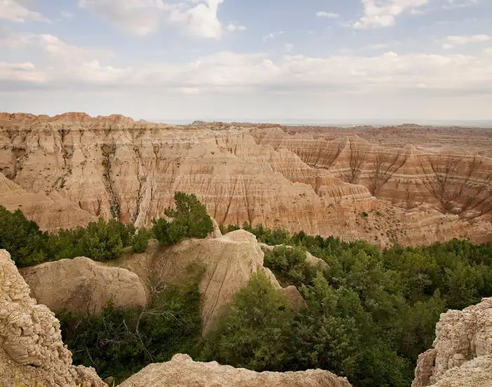 South Dakota Badlands aerial view of sedimentary layers of rocks with stripes with sections of thick forestry made up of green trees.