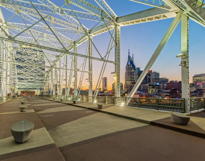 View from inside the white John Seigenthaler Pedestrian Bridge In Tennessee looking out into a scenic cityscape and waters.