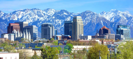 Cityscape of Salt Lake City, Utah with buildings in front of large snow-capped mountains on a sunny day with clear skies.