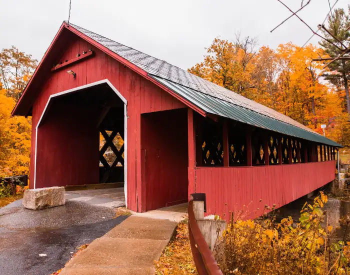 Red covered bridge surrounded by autumn foliage in Vermont.