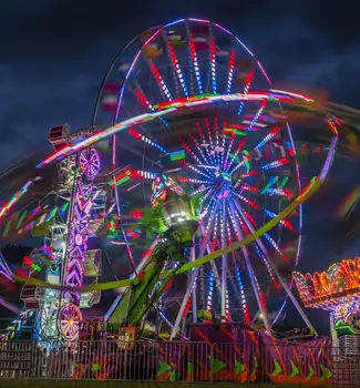 Spinning lit up ride in front of a tall ferris wheel in Champlain Valley Exposition fair in Vermont at night.