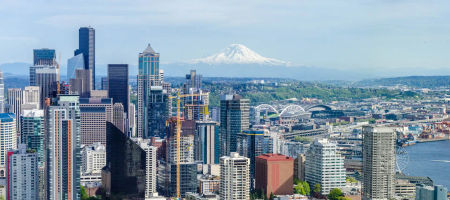 Aerial view of Seattle, Washington during the day overlooking the city, mountains, buildings, bridges, ferris wheels, and the waterfront.