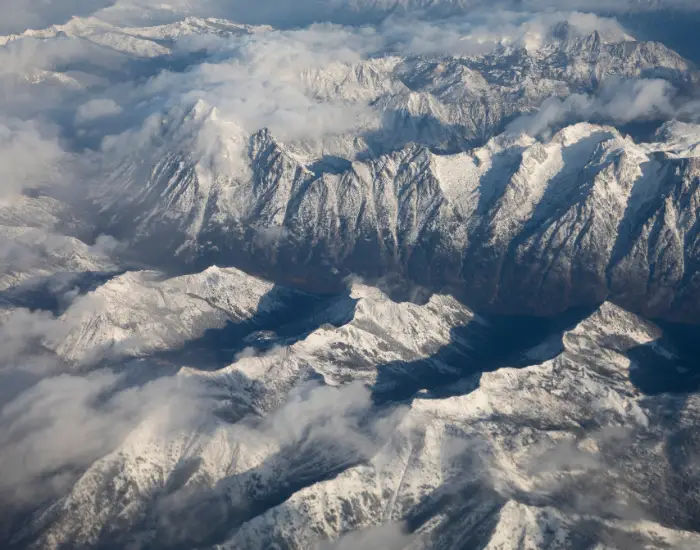 Aerial view of Mount Stuart in the Alpine Lakes Wilderness area of the Cascade Range Mountains covered by snow, clouds, and smoke.