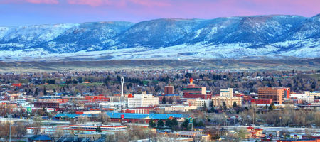 Aerial city view of Caster, Wyoming in Natrona County with buildings surrounded by leaf-less trees in Winter with snow-capped mountains in the background.