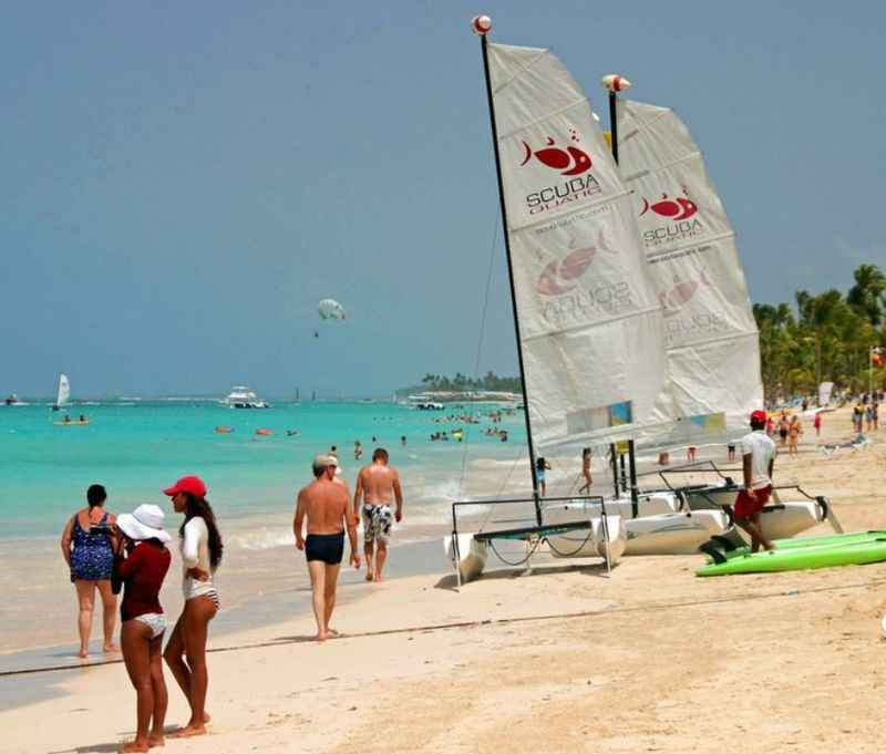 a group of people walking on a beach next to sailboat