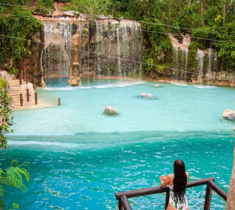 a woman on a ledge looking at a waterfall