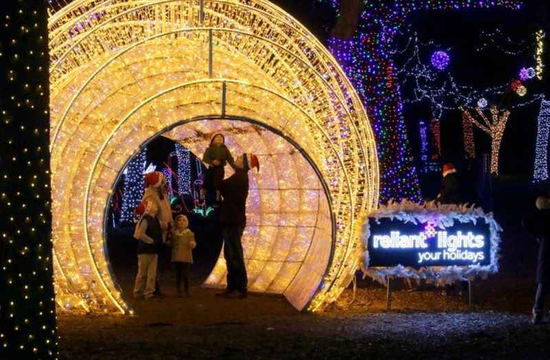 people walk through a tunnel covered in lights