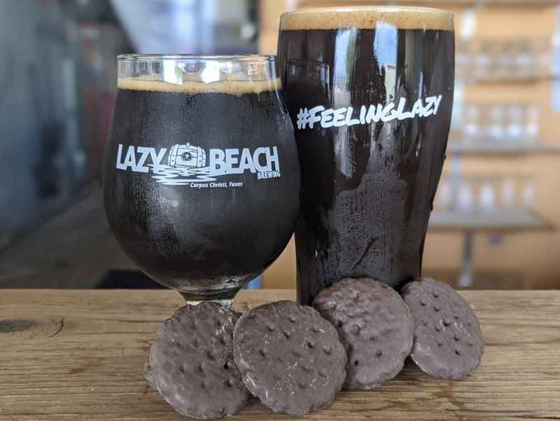 two glasses of beers next to a chocolate coated cookie