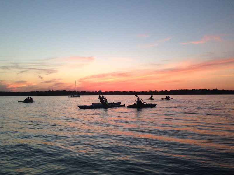 a group of people are in the water at sunset