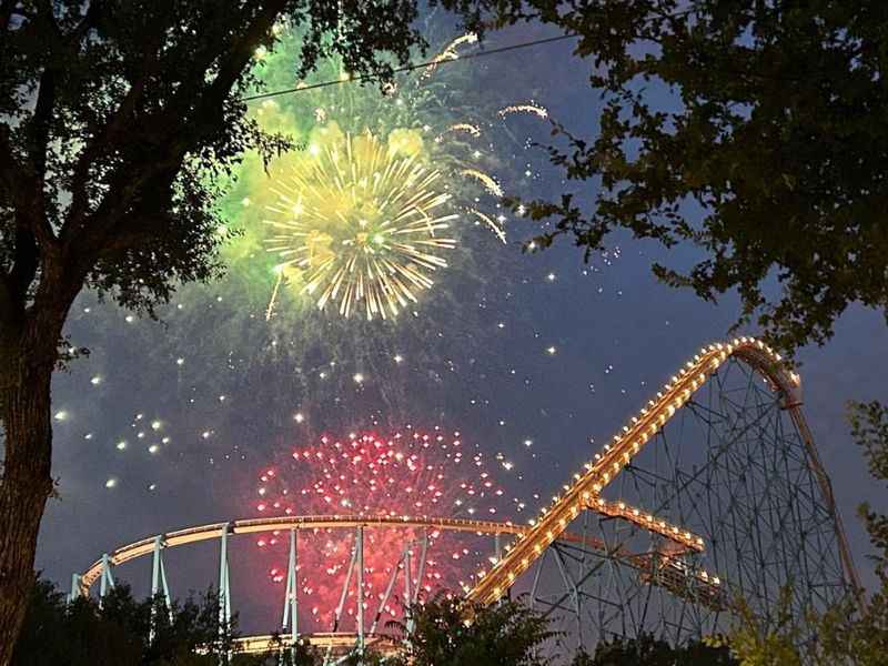 fireworks are lit up the sky above a roller coaster