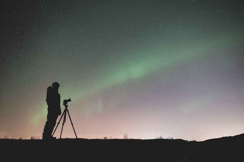 a man is standing on a hill looking at the aurora