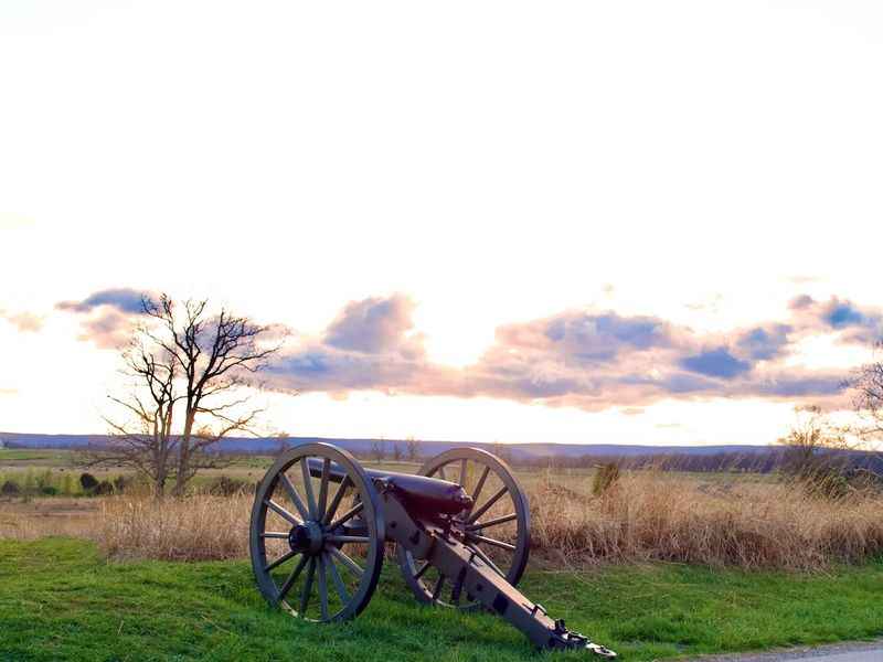 a cannon sits in the grass near a road