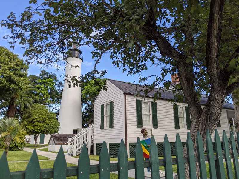 a white house with a green fence and white lighthouse