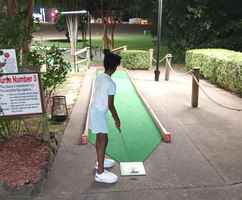 a young boy playing mini golf at night time