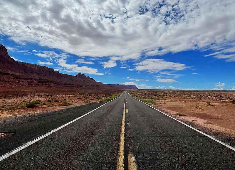 a long road with a blue sky and clouds