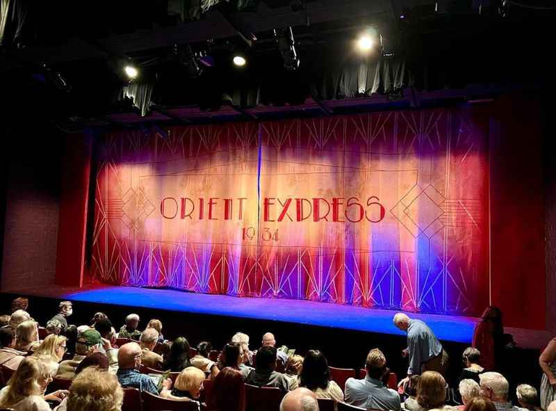 people sitting on chairs and a stage with red curtain