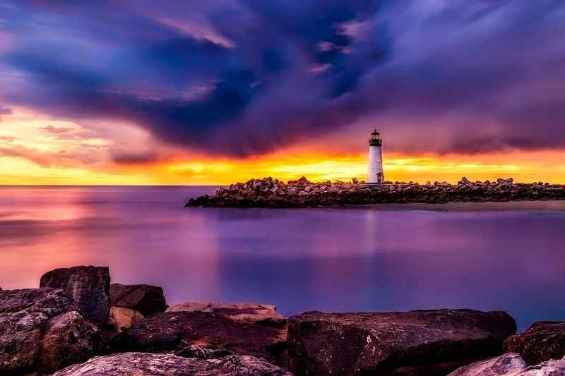 a lighthouse sits on the rocks at sunset