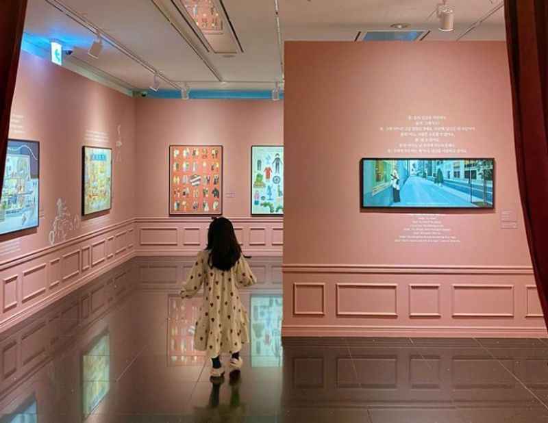 a woman walking through a museum with pink walls