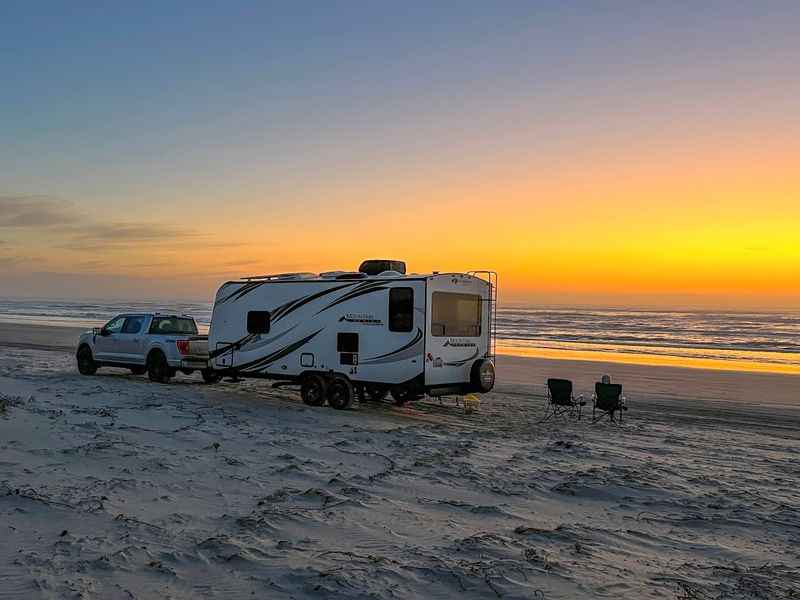 a white rv parked on the beach at sunset