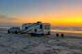 a white rv parked on the beach at sunset