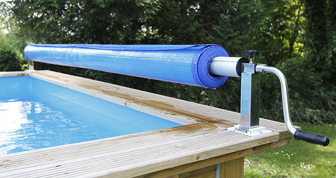 Enrouleur de bâche fixé sur la margelle d'une piscine en bois