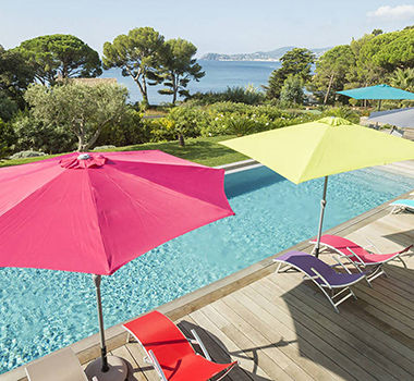 Parasols rose et vert qui ombragent des chaises longue au bord d'une piscine